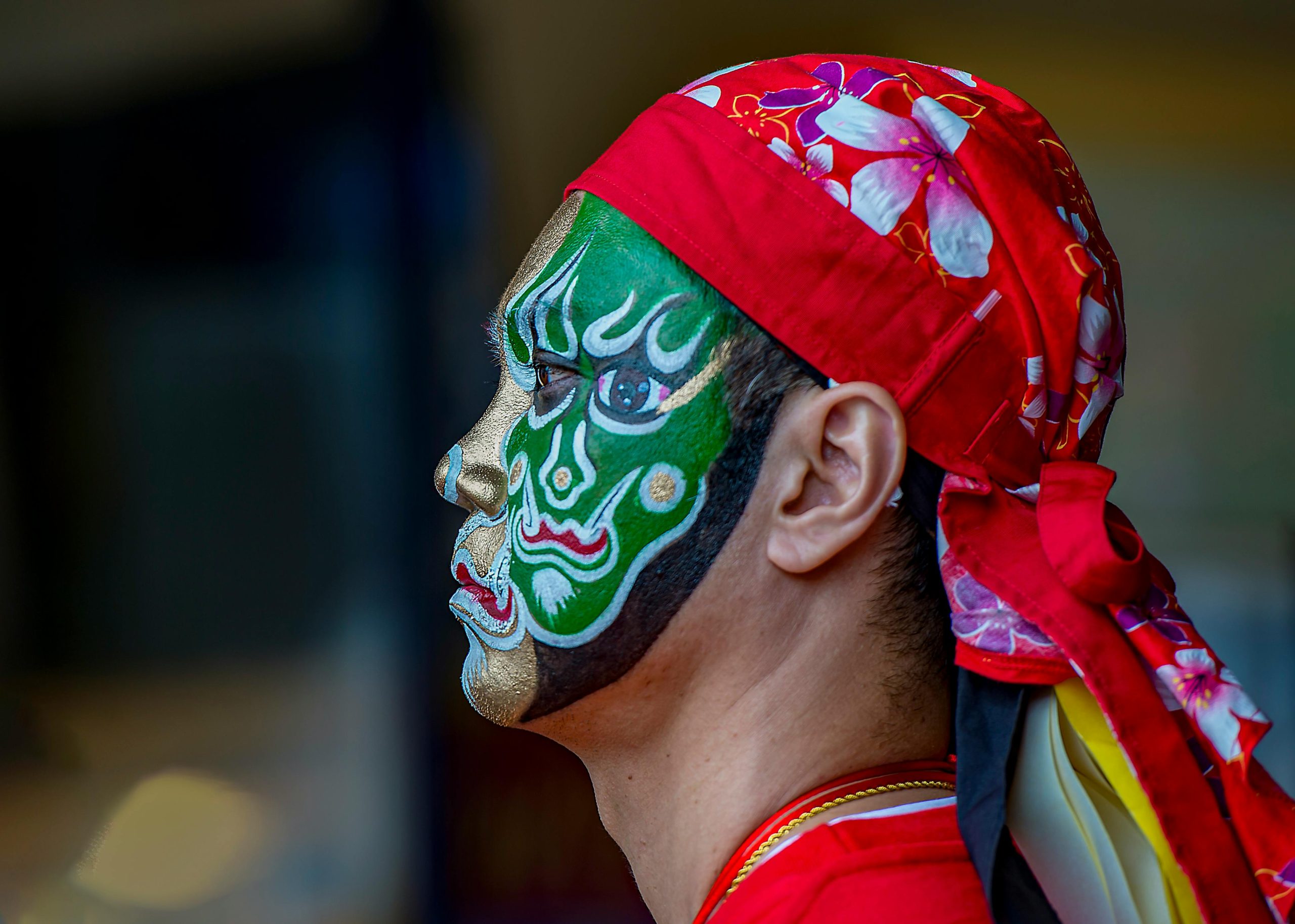 Close-up side profile of a man with vibrant face paint and red bandana, captured in Taipei.